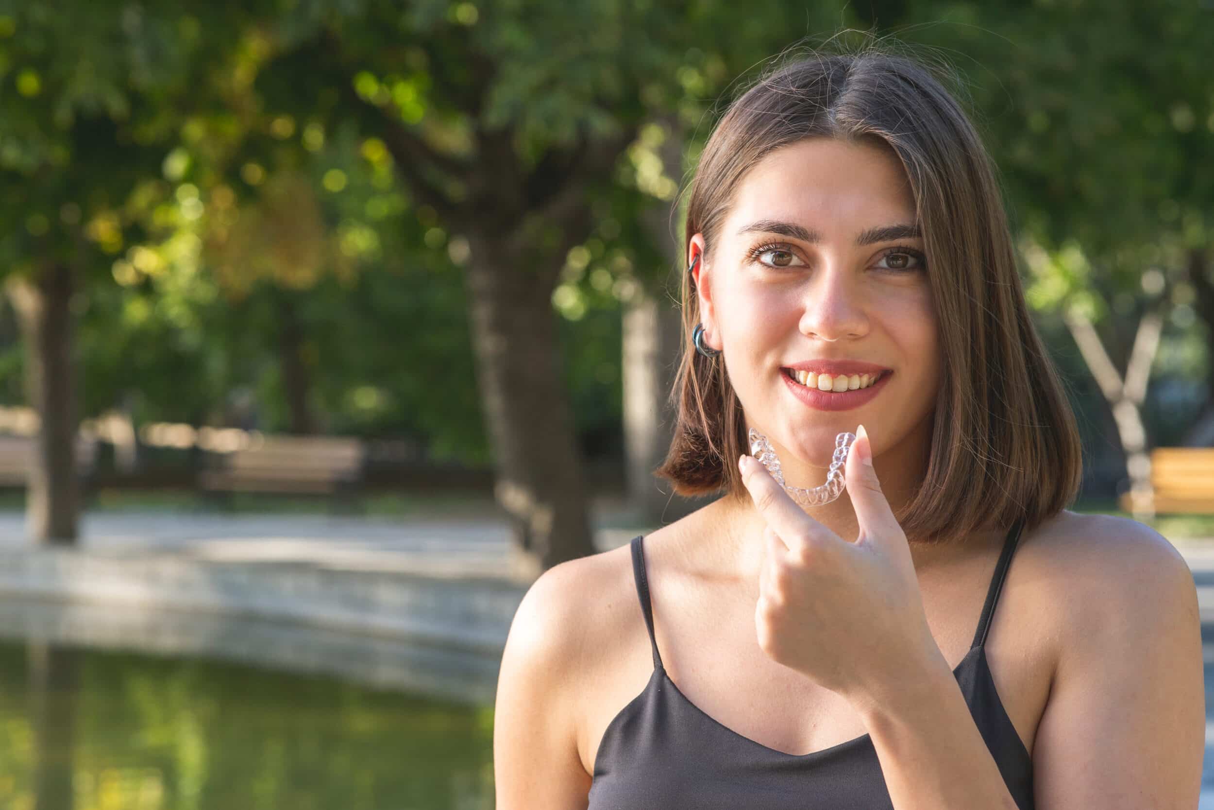 Happy young woman putting in her Invisalign aligners on the go after eating
